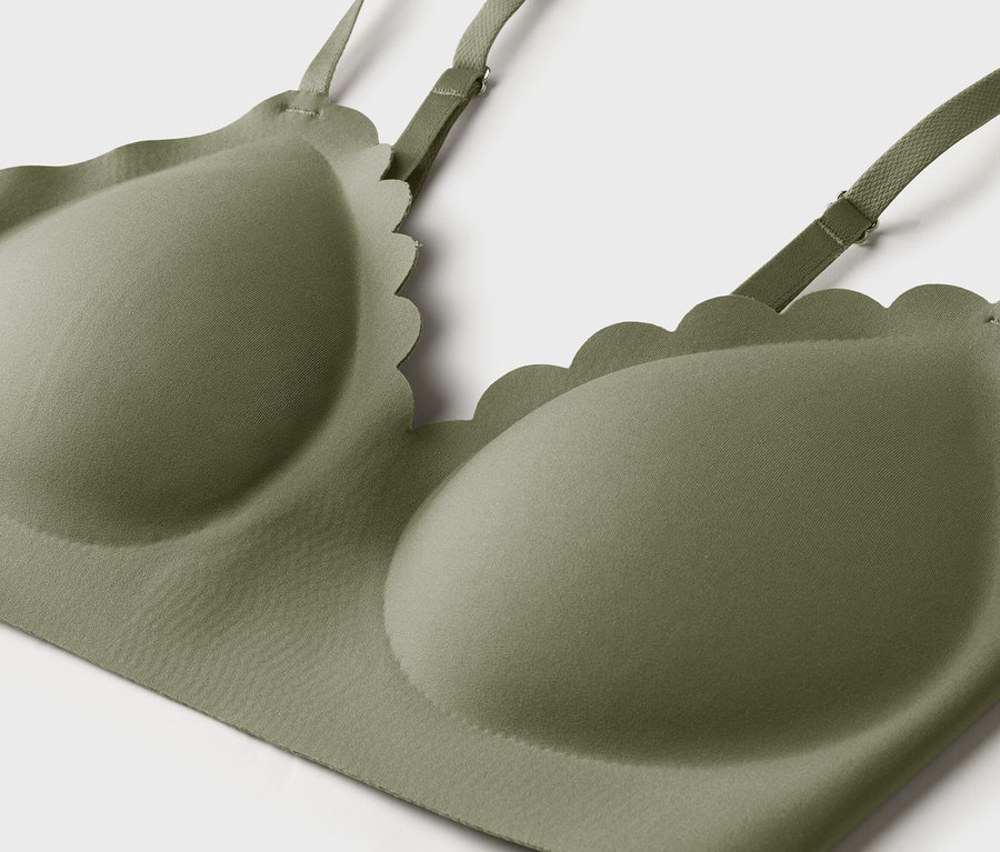 Gros plan d'un soutien-gorge vert olive avec des bords ondulés et des bretelles réglables sur fond blanc.