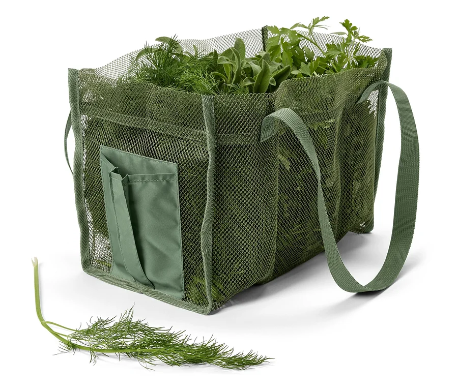 Un sac en filet vert est rempli d'herbes fraîches, notamment de l'aneth, de la sauge et du persil. Une tige d'aneth est posée devant.