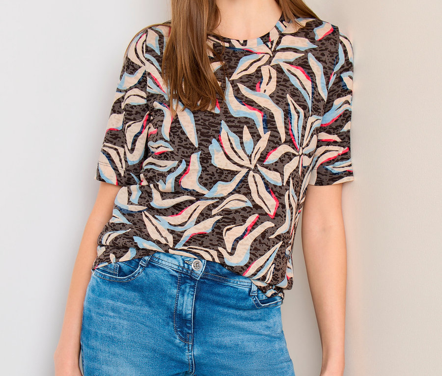 Femme en T-shirt manches courtes CECIL à motif bleu-rose-beige, jean bleu, tenant un sac noir.