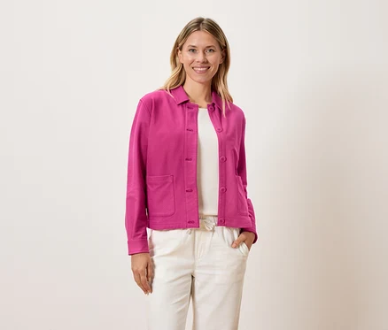 Femme portant une veste rose sur un haut blanc et un pantalon crème.