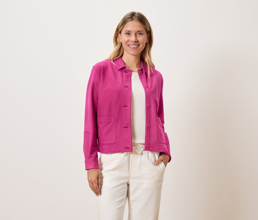 Femme portant une veste rose sur un haut blanc et un pantalon crème.