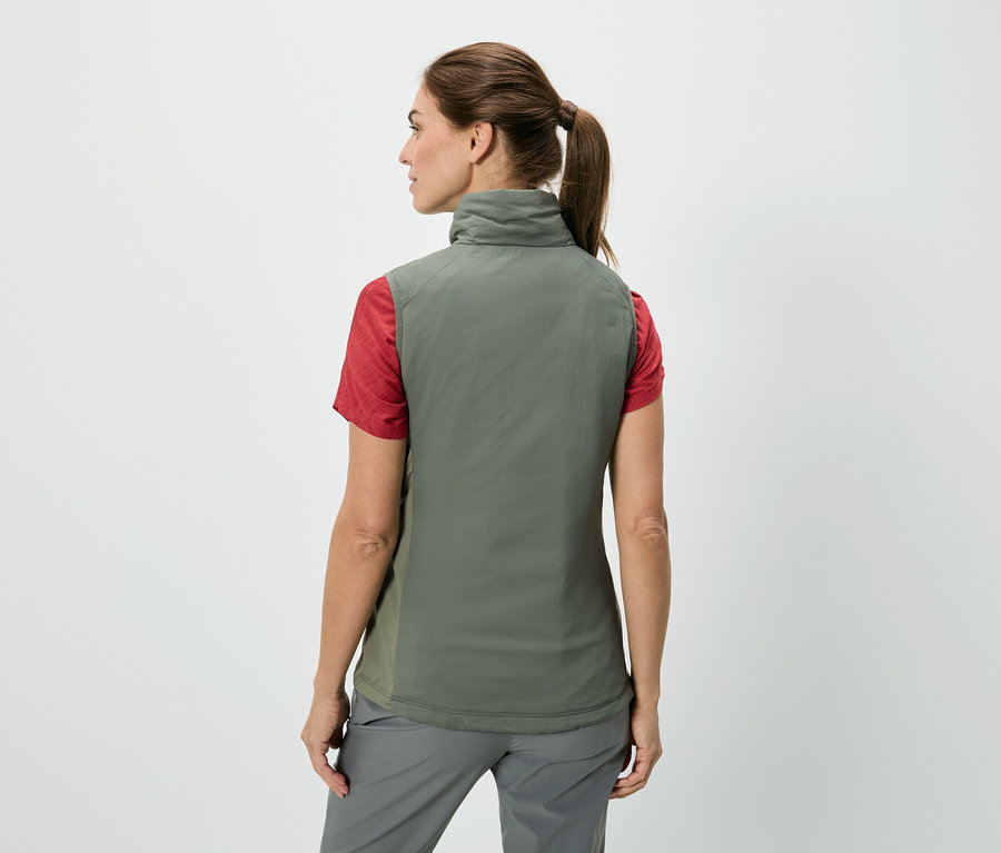 Vue arrière d'une femme avec une queue de cheval portant un gilet vert olive sur un t-shirt rouge et un pantalon gris sur un fond blanc.