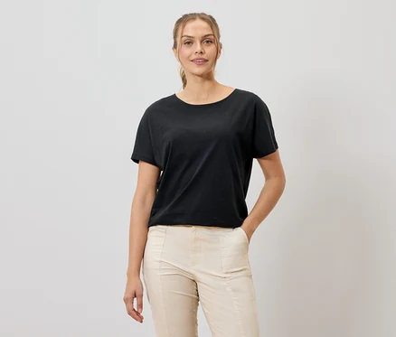 Femme portant un t-shirt noir et un pantalon beige souriant à la caméra.