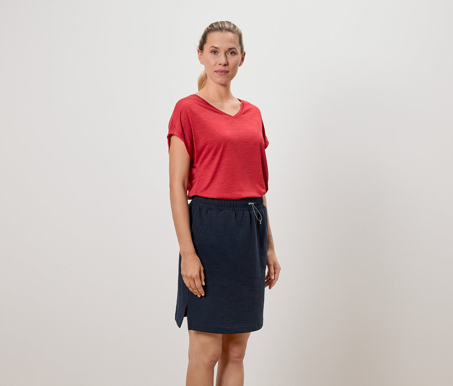 Femme portant un t-shirt rouge et une jupe bleu marine.