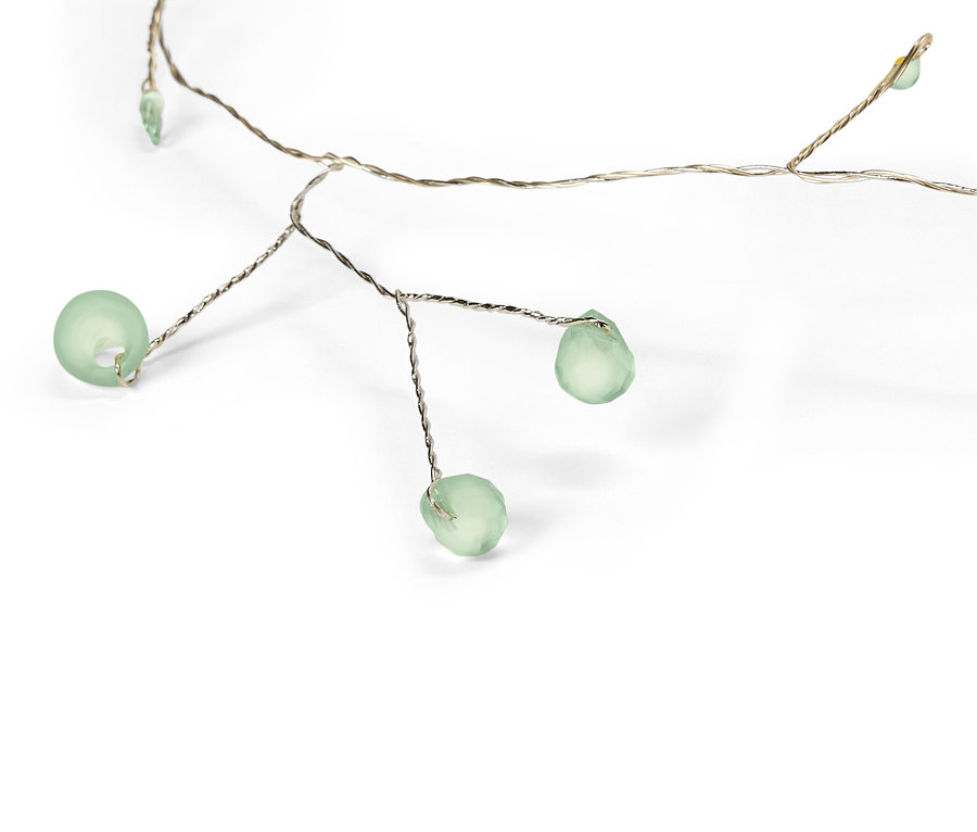 Gros plan d'une guirlande lumineuse avec des perles de verre verdâtres sur un fil argenté sur fond blanc.