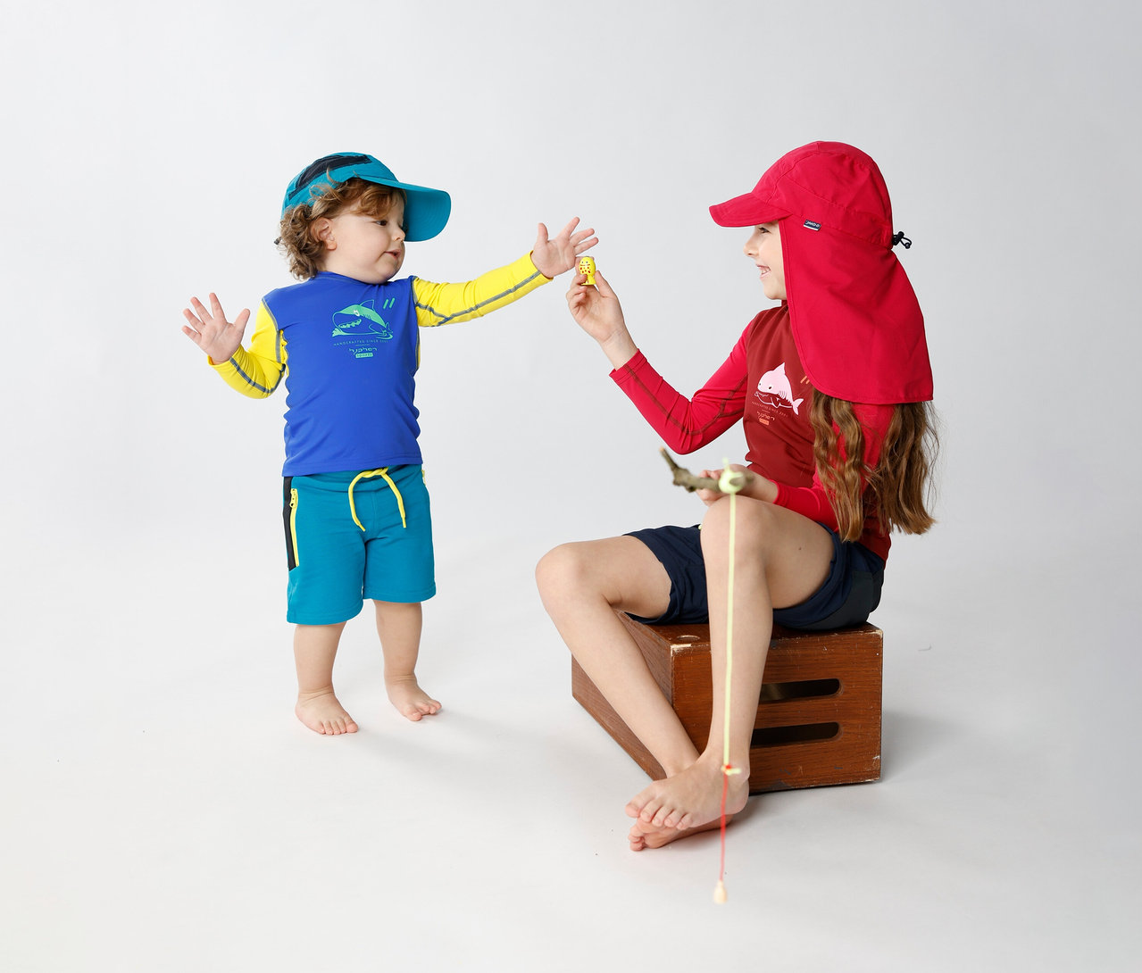 Un enfant tend un objet à un enfant assis. L'enfant assis porte une Casquette JAKO-O avec protège-nuque, raisin.