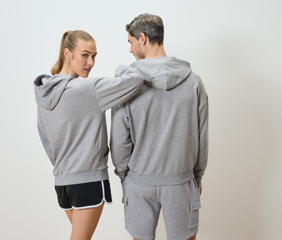 Une femme aux cheveux blonds et un homme aux cheveux gris portent des pulls à capuche gris et des shorts.