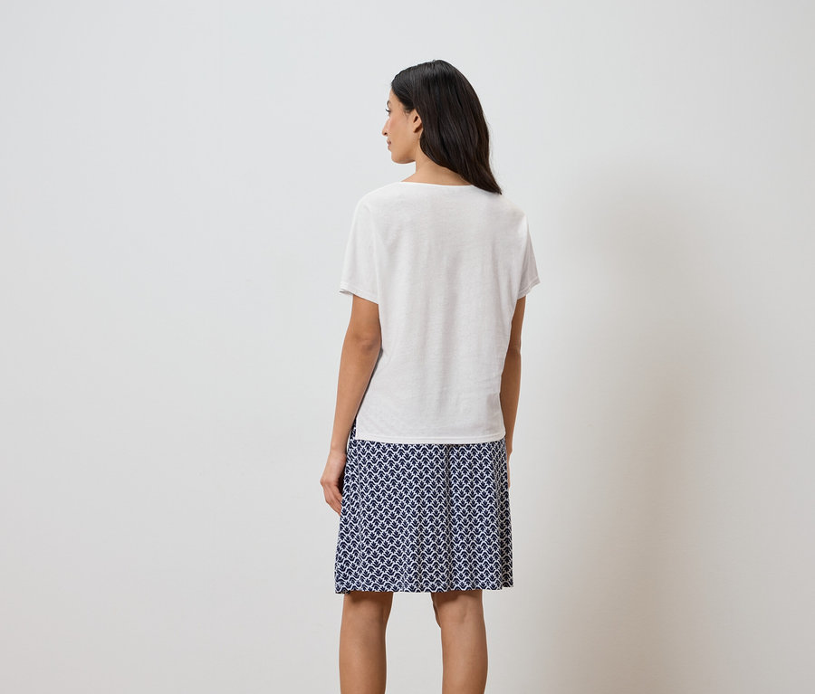 Vue arrière d'une femme aux cheveux foncés portant un t-shirt blanc et une jupe à motifs bleus.