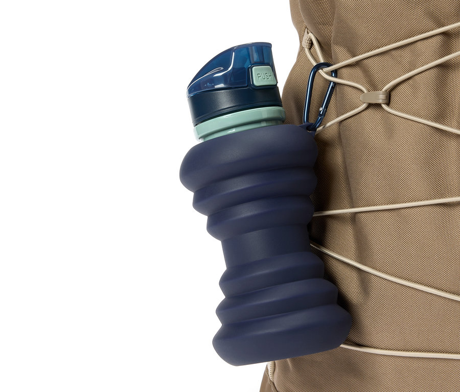 Gros plan d'une gourde compressible bleue attachée à un sac à dos beige avec un mousqueton.