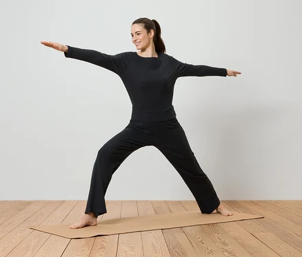 Une femme en vêtements de sport noirs fait du yoga sur un tapis de yoga.