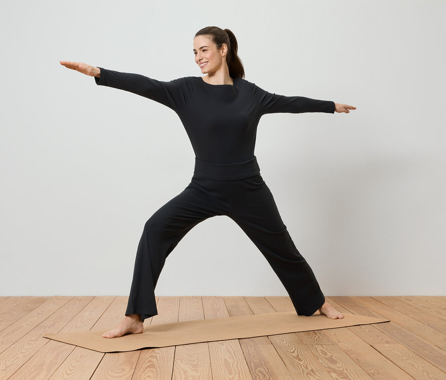 Une femme en vêtements de sport noirs fait du yoga sur un tapis de yoga.