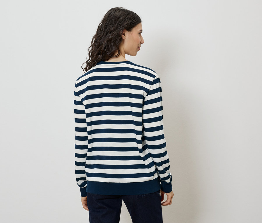Vue arrière d'une femme aux longs cheveux ondulés et foncés, portant un pull rayé bleu marine et blanc et un jean foncé.