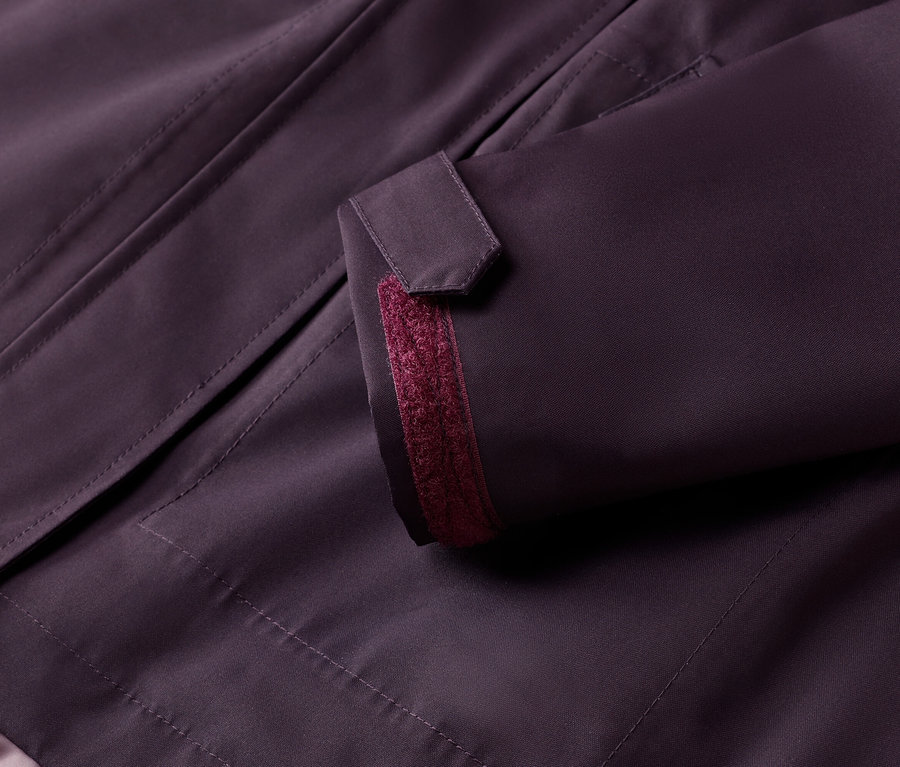 Gros plan sur une veste aubergine avec un bouton sur la manche et un accent bordeaux.