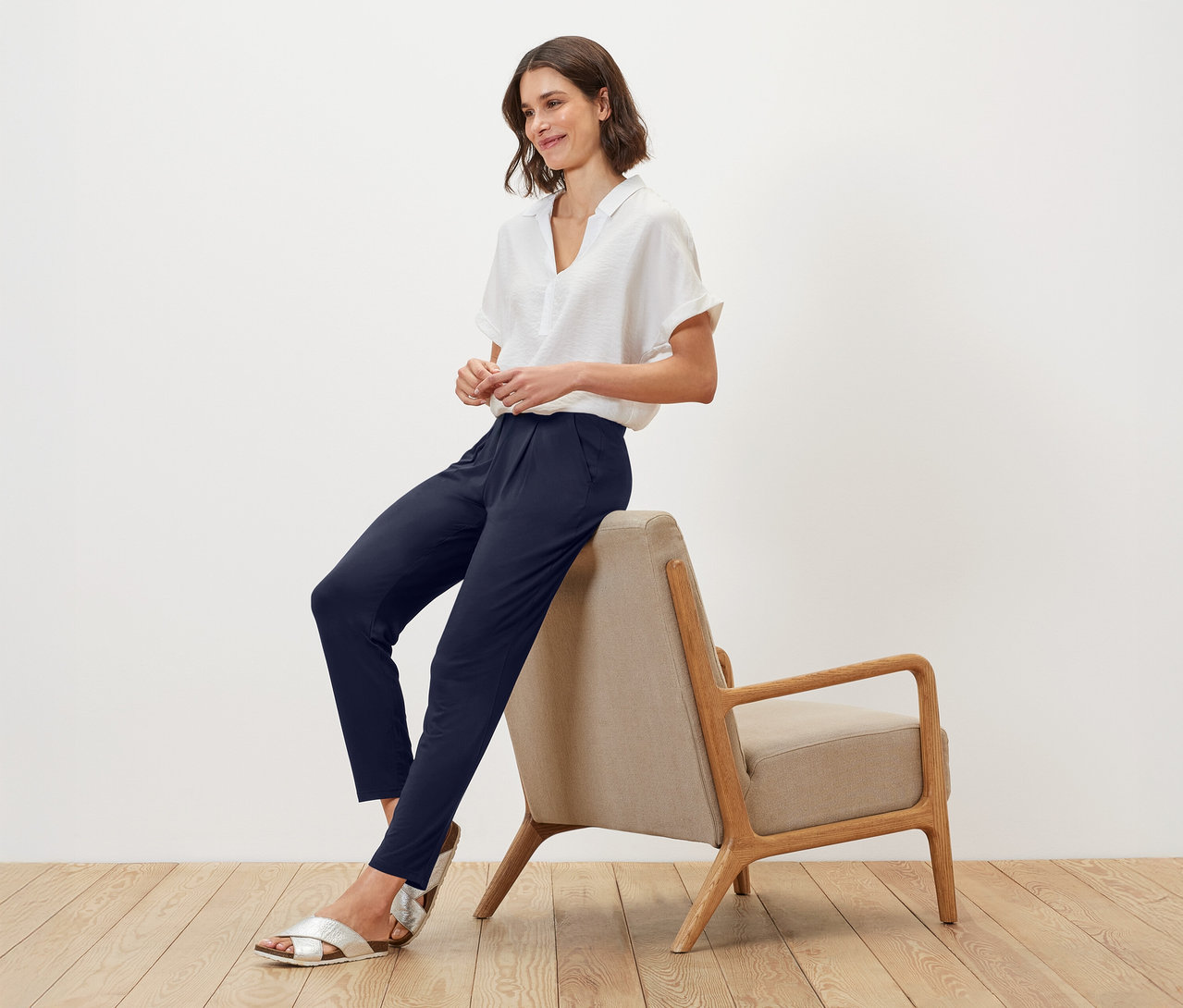 Femme assise sur une chaise, portant un chemisier blanc et un pantalon bleu marine.