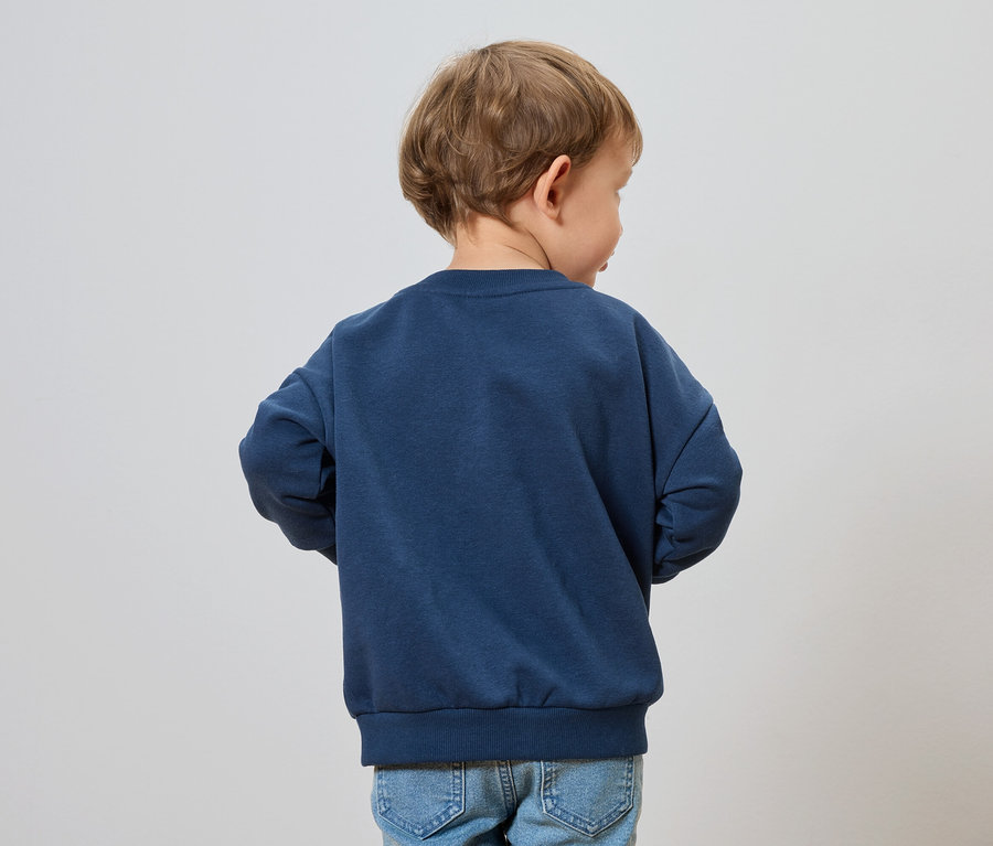 Un enfant aux cheveux blonds porte un sweat-shirt bleu marine et un jean.
