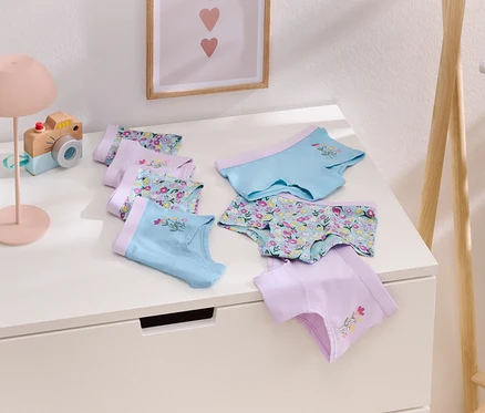 Sur une table blanche sont disposés plusieurs slips pour filles de couleur lilas et bleu clair avec un motif floral.