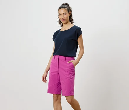 Femme portant un t-shirt foncé et un short rose sur un fond blanc.