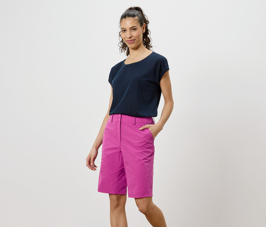 Femme portant un t-shirt foncé et un short rose sur un fond blanc.