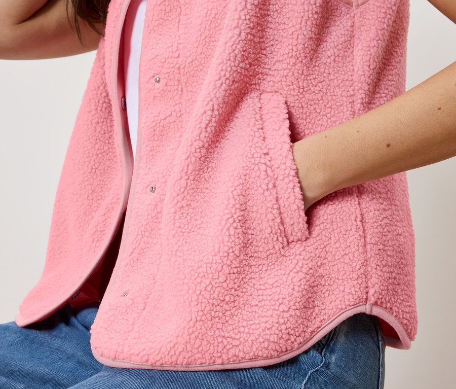 Femme avec une main dans la poche du gilet sans manches en peluche teddy porté sur un haut blanc et un jean.
