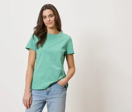 Femme aux longs cheveux bruns portant un t-shirt vert et un jean bleu.