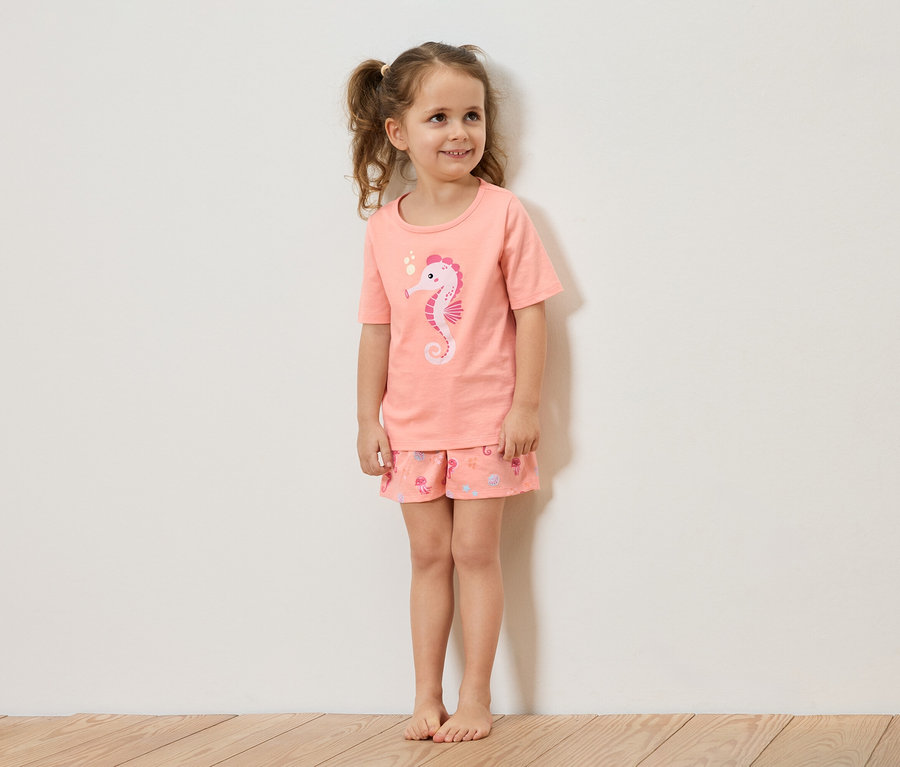 Fillette avec des tresses porte un pyjama couleur saumon avec un motif d'hippocampe.