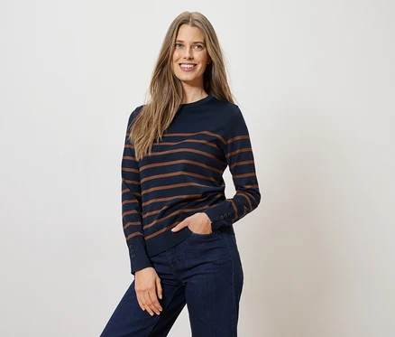 Femme portant un pull rayé bleu marine et un jean, une main dans la poche.