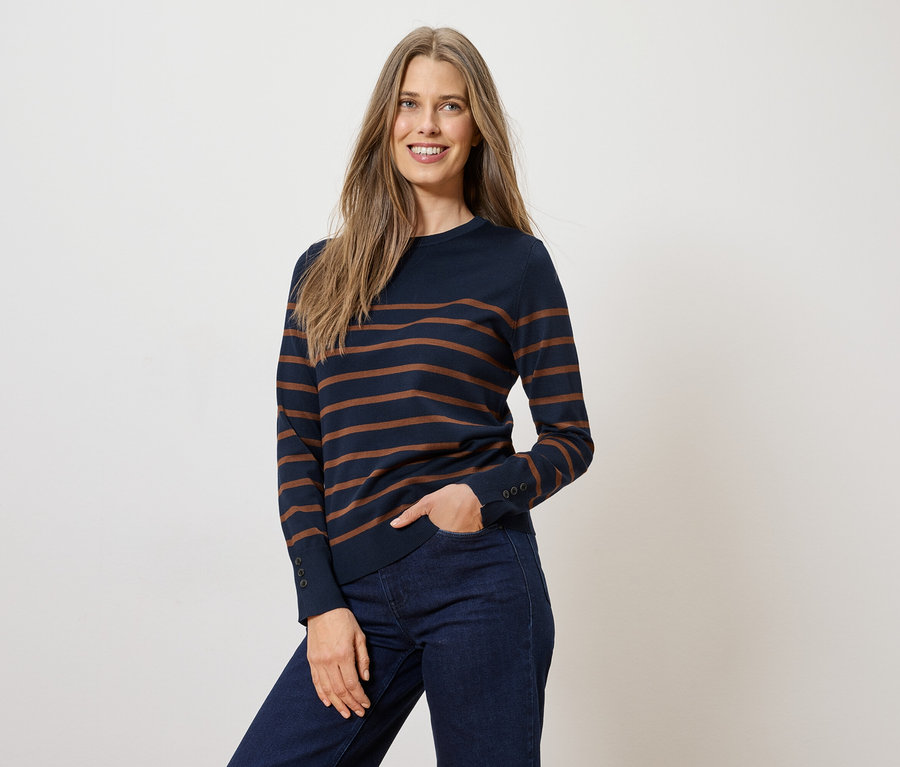 Femme portant un pull rayé bleu marine et un jean, une main dans la poche.