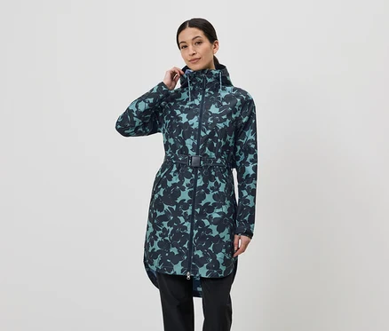 Une femme aux cheveux relevés porte un long imperméable à fleurs avec une ceinture et une capuche, ainsi qu'un pantalon noir sur un fond blanc.