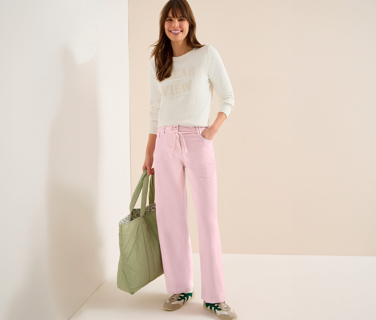 Une femme avec un sac porte un haut clair et un jean CECIL « Neele » rose.