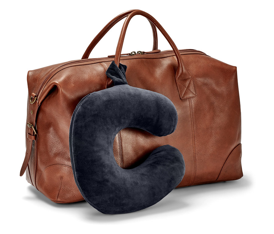 Un coussin de nuque bleu foncé est suspendu devant un sac de voyage marron.