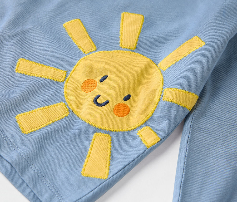 Gros plan sur un vêtement bleu clair orné d'un soleil jaune cousu.