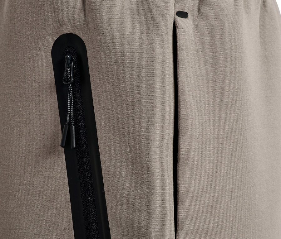 Gros plan d'un pantalon de jogging beige avec une poche zippée noire et une poche ouverte.