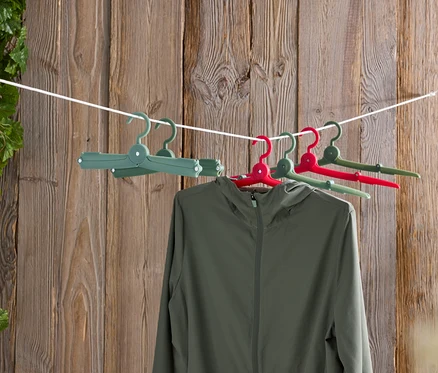 Une veste verte suspendue à des cintres colorés sur une corde à linge devant un mur en bois.
