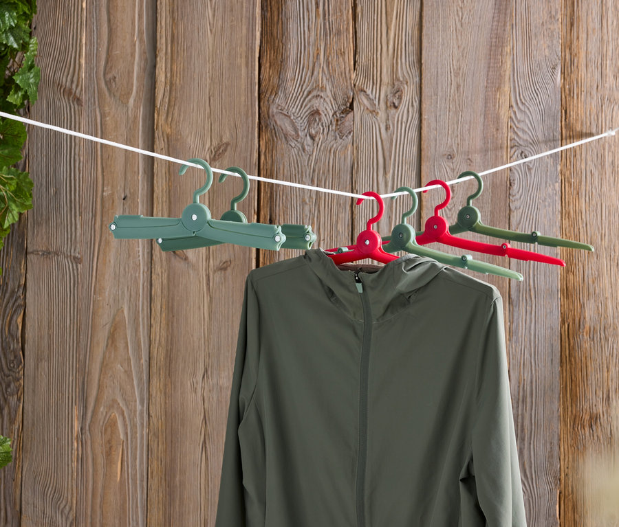 Une veste verte suspendue à des cintres colorés sur une corde à linge devant un mur en bois.