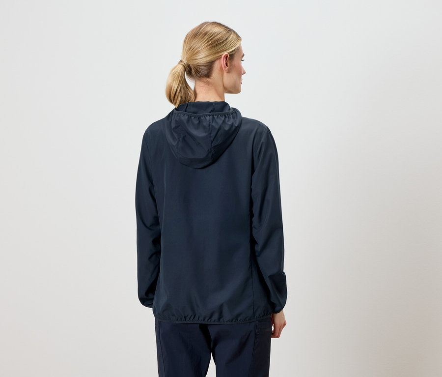 Vue arrière d'une femme aux cheveux blonds portant une veste à capuche bleu marine et un pantalon bleu marine.