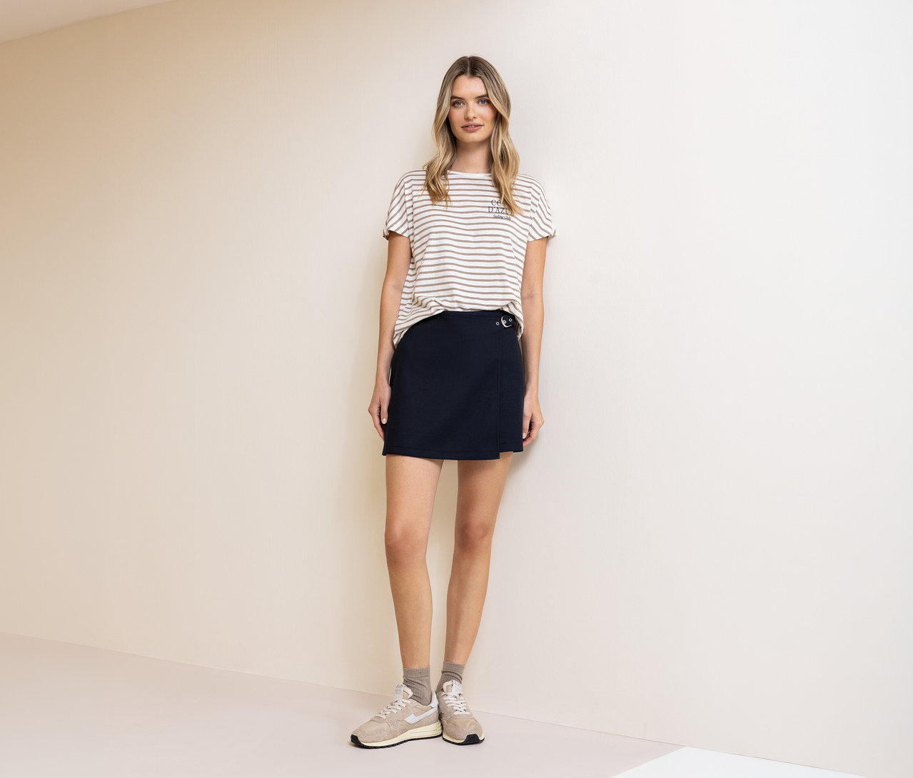 Une femme porte un t-shirt Street One, beige et blanc, et une jupe-culotte Street One. Des chaussettes et des baskets complètent sa tenue.