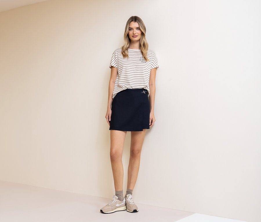 Une femme porte un t-shirt Street One, beige et blanc, et une jupe-culotte Street One. Des chaussettes et des baskets complètent sa tenue.