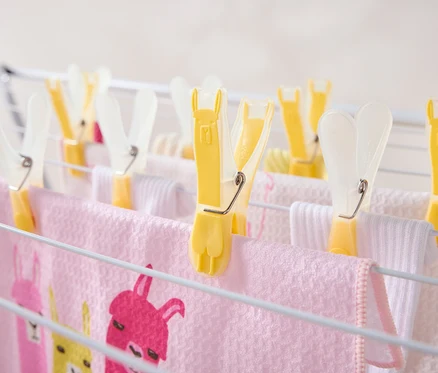 Des pinces à linge jaunes maintiennent des serviettes roses et blanches sur un séchoir.