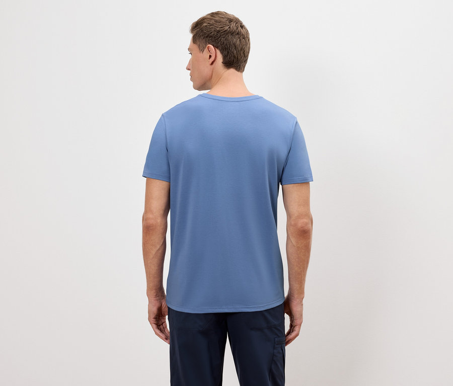 Un homme se tient dos à la caméra, portant un t-shirt bleu et un pantalon bleu marine.