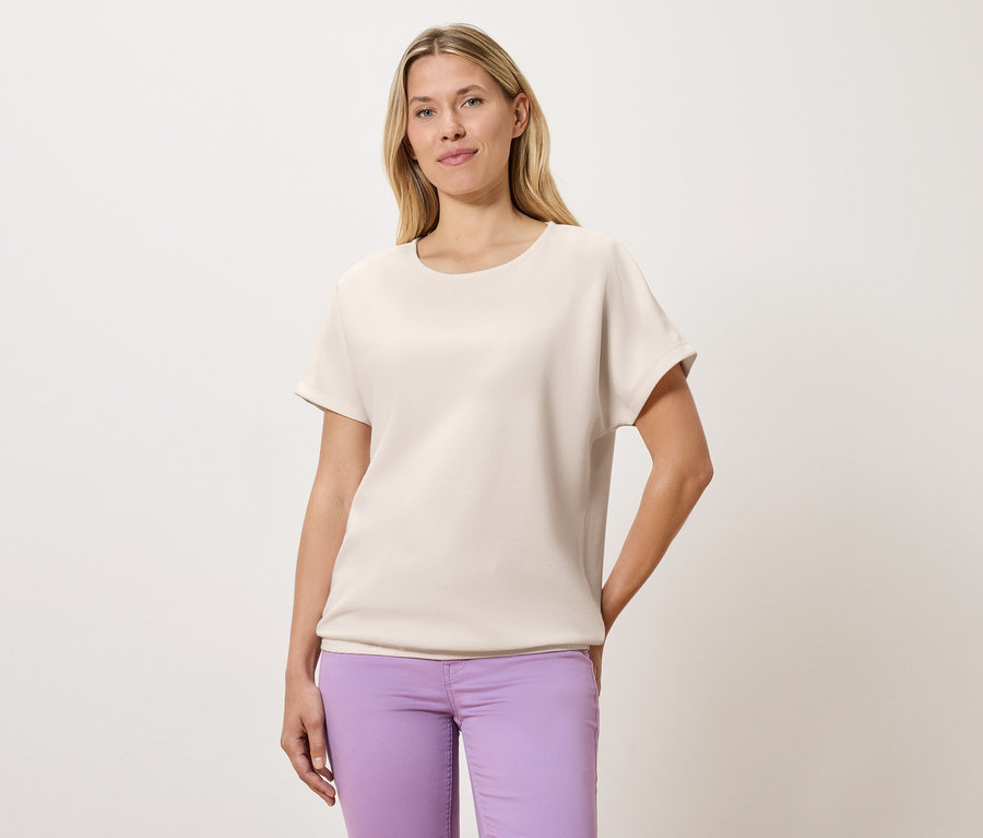 Une femme porte un t-shirt clair et un pantalon violet.