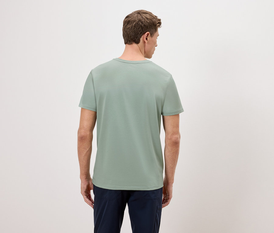 Un homme se tient dos à la caméra, portant un t-shirt vert et un pantalon bleu.