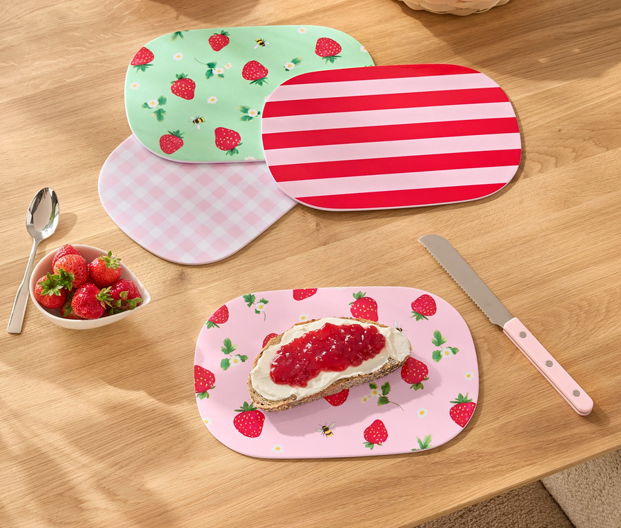 Sur une table en bois sont disposées quatre assiettes à motifs différents, un petit bol de fraises, un pot de confiture de fraises, un couteau à pain et une corbeille à pain.