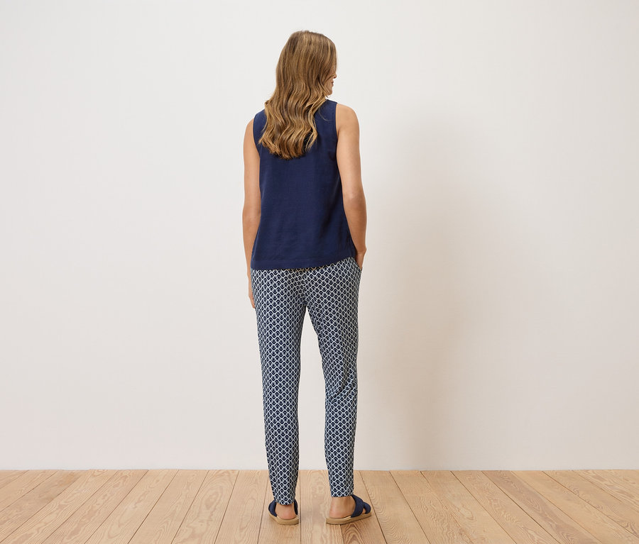 Une femme se tient dos à la caméra, portant un haut bleu marine et un pantalon à motifs.