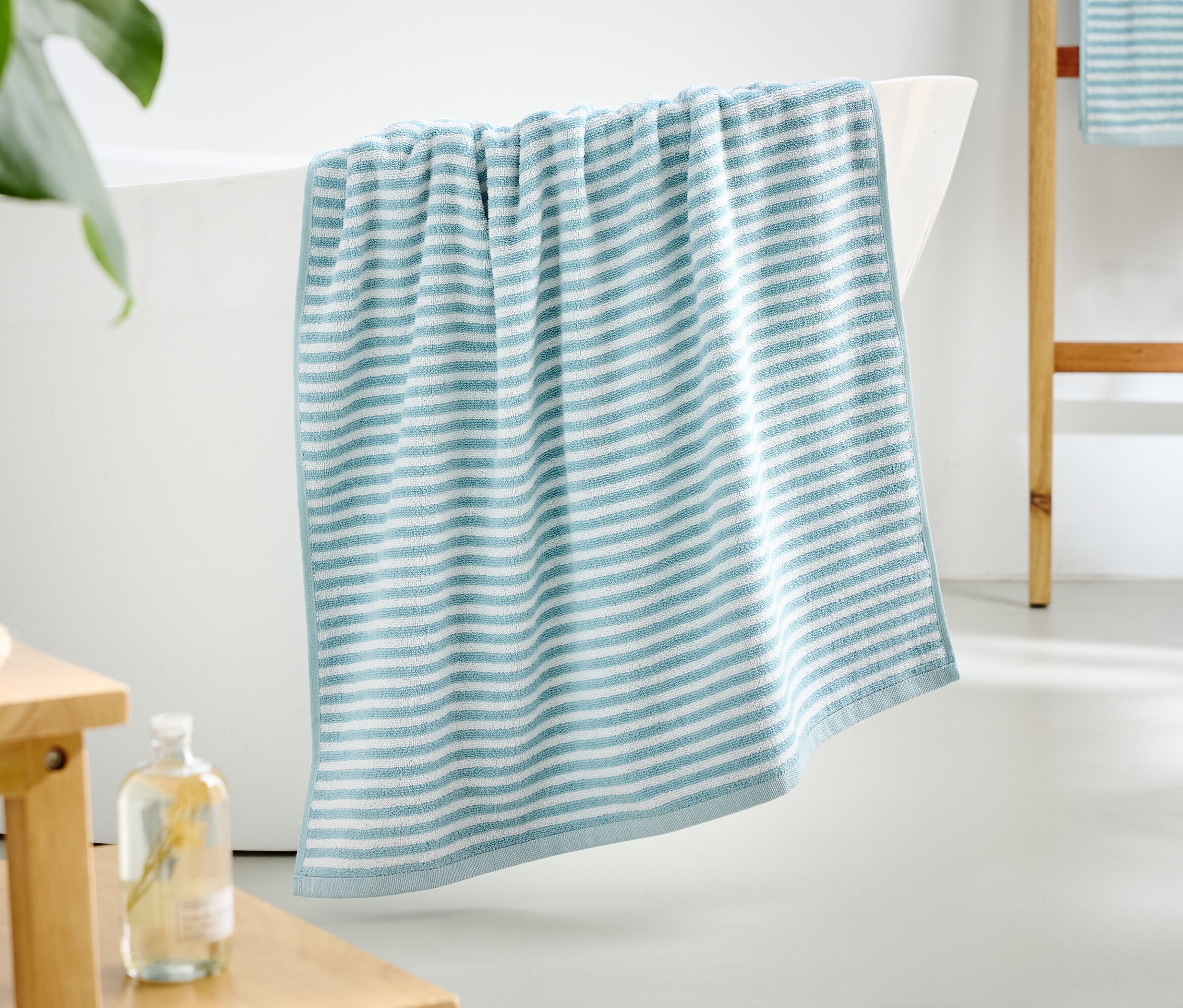 Une serviette rayée bleu et blanc est accrochée au bord d'une baignoire.