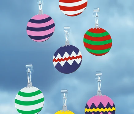 Sept décorations de boules de Noël circulaires de différentes couleurs suspendues à des clips transparents sur un fond bleu.