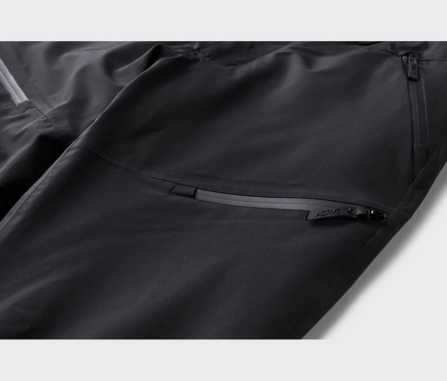 Gros plan d'un pantalon noir avec des poches zippées et une bande réfléchissante. Une tirette de fermeture éclair est marquée "ACTIVE".