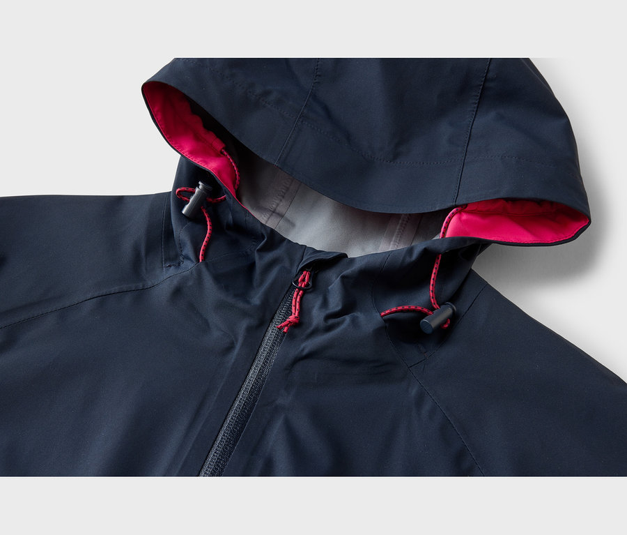 Veste bleu foncé avec capuche, doublure rose, cordons de serrage rouges avec stoppeurs noirs et fermeture éclair.