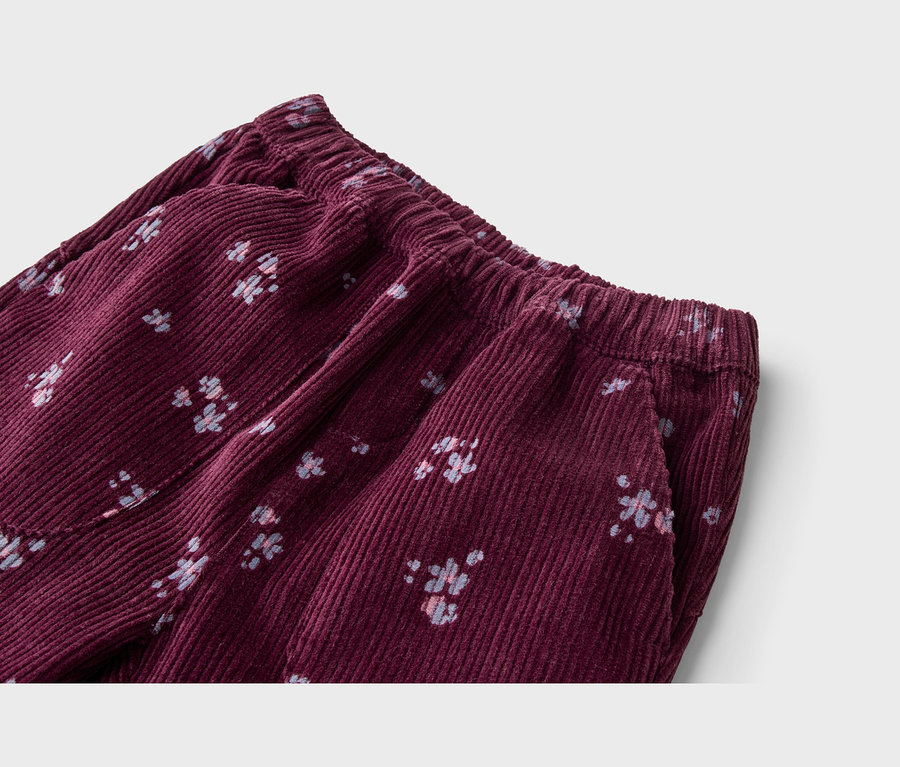 Gros plan d'un pantalon en velours côtelé bordeaux avec une taille élastique et des poches latérales, orné d'un petit motif floral clair.