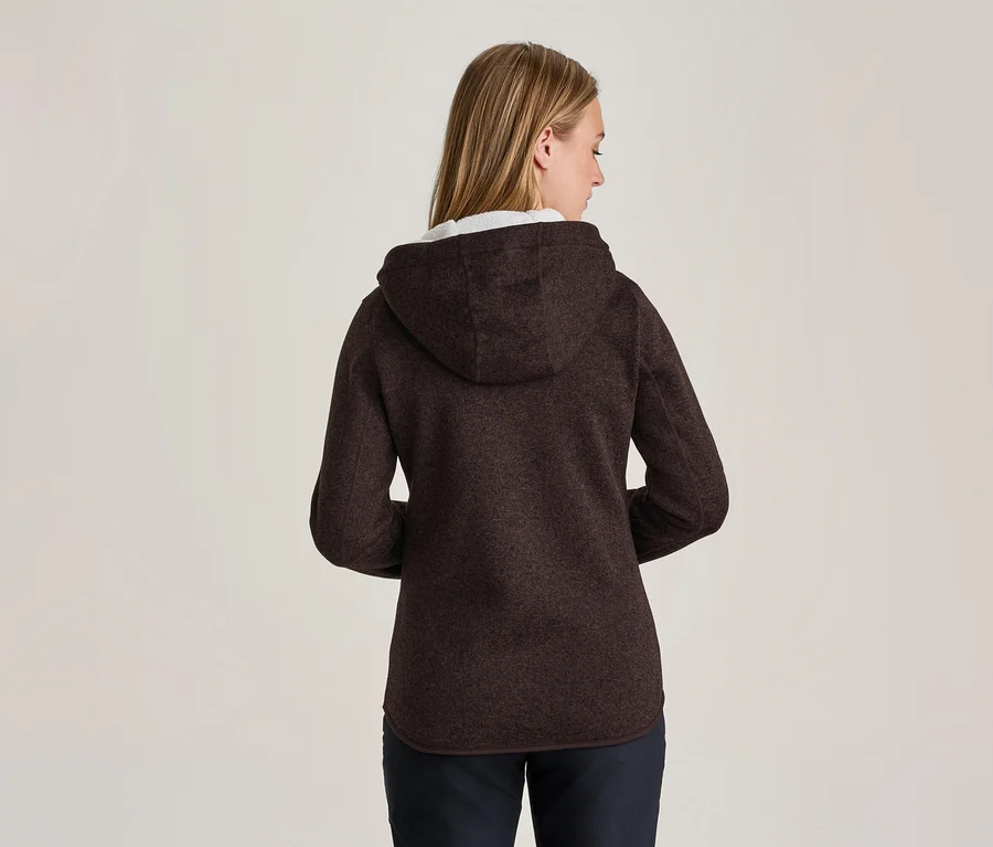 Femme vue de dos, portant une veste polaire à capuche marron foncé et un pantalon foncé. Ses cheveux blonds sont visibles.