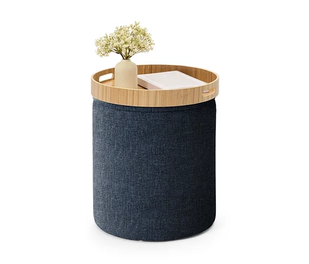 Pouf de rangement cylindrique bleu foncé avec un plateau en bois, sur lequel se trouvent un vase de fleurs blanches et un livre.
